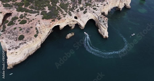Aerial drone view of Benagil Sea Caves and Atlantic Ocean coastline in Benagil, Algarve, Portugal, Europe. Dark blue ocean, boats, and coastal landscape