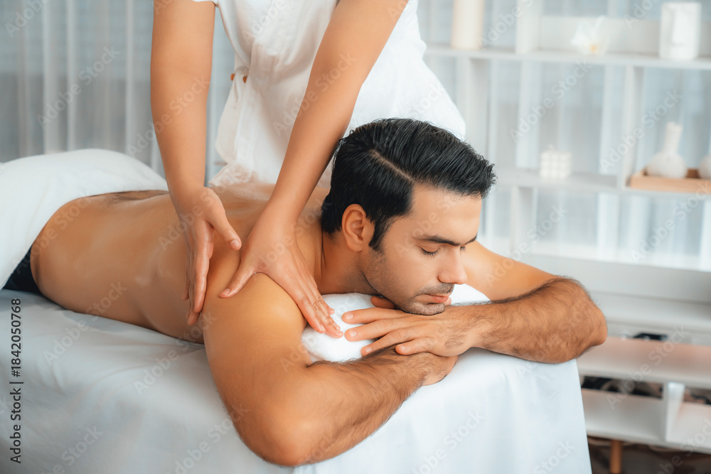 Naklejka premium Caucasian man customer enjoying relaxing anti-stress spa massage and pampering with beauty skin recreation leisure in day light ambient salon spa at luxury resort or hotel. Quiescent