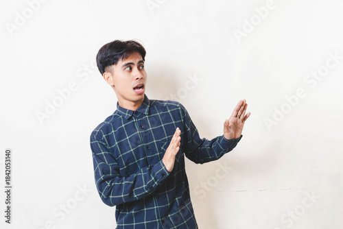 фотографія Surprised young man stepping back with defensive hand gesture on white background, showing reaction, fear, or avoiding situation