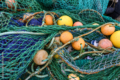 Large pile of industrial grade fishing nets, rusty metal cables, and yellow and orange floats, commercial fishing industry, storage at port in Scotland, UK
