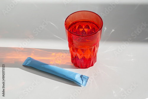 Single serving drink mix sachet next to glass, for instant beverage preparation.