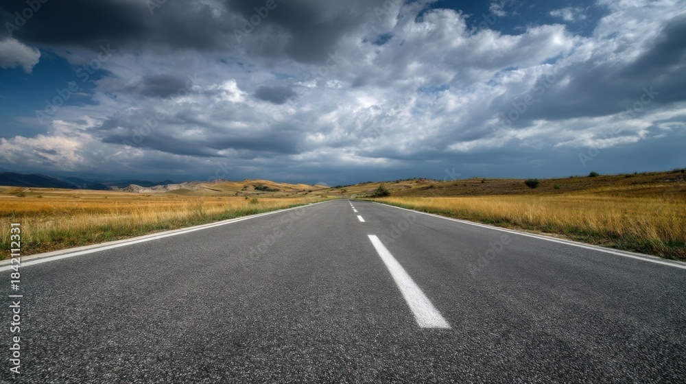 Naklejka premium A straight paved highway cuts through wild golden grasslands under clear blue skies,