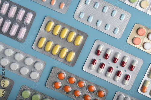 Various medicine capsules, pills and tablets in blister packs isolated on blue background, top view. Health and medicine concept.