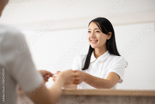 Female medical receptionist in white uniform receiving card at front desk