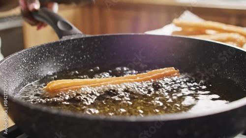 Removing churro from hot oil with tongs during deep frying cooking preparation