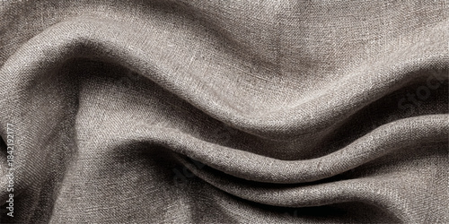 Close up of natural linen fabric with soft folds and textured surface in neutral taupe color