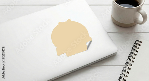 Mockup de pegatina adhesiva beige en blanco pelándose sobre la tapa de un ordenador portátil en un escritorio de madera blanca con café. Plantilla de mockup de sticker vacío en laptop para diseño de m