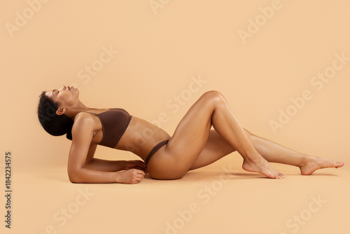 Fotografi Young black woman lying in fitness inspired pose on beige background