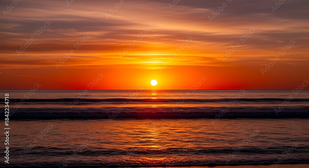 Fototapeta premium Vibrant orange sunset over calm ocean waves with golden light reflection