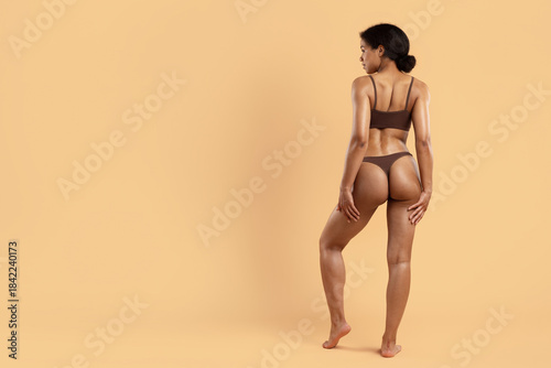 фотографія Rear view of fit young black woman in brown underwear on beige studio background