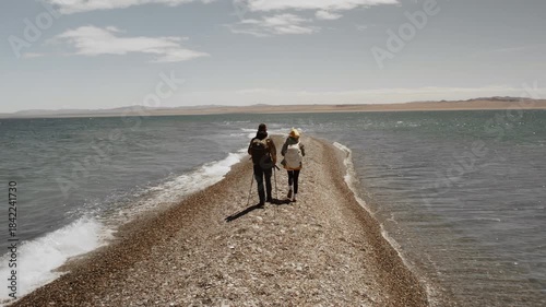Trekkers with backpacks walk to the water of a high-mountain lake in the Gobi Desert, Mongolia, Mongol Els region. Outdoor activity on sunny day at summer vacation, trip in the desert