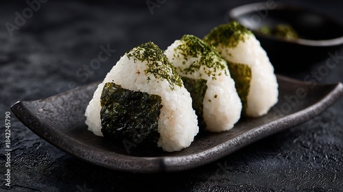 Close up view of Japanese onigiri rice balls seaweed wrapping served on ceramic plate against dark black textured backdrop