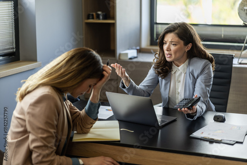 Billede på lærred Two businesswomen engage in a tense discussion during a financial meeting in a m