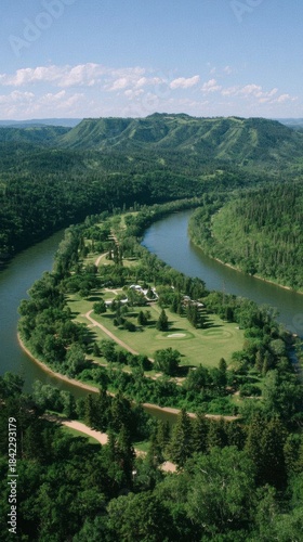 Aerial view of a wide winding river curving around a dense forested peninsula under a bright blue sky