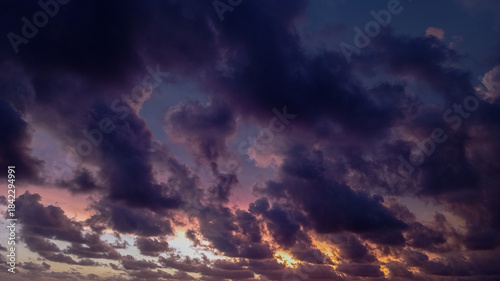 Dramatic dark storm clouds gather over a tranquil beach at dusk, reflecting soft golden light onto the crashing ocean waves