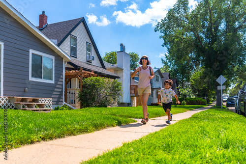 Фотография Mother and son running on sidewalk in suburban neighborhood