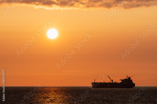 Golden Baltic Sea Sunset Silhouette of an Oil Tanker or Cargo Ship Cruising Near the Estonian Coastline with Bright Sun.