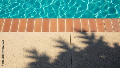 Vibrant blue swimming pool water with brick coping and dappled sunlight on the deck