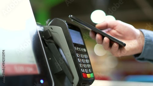 Close up man At Counter Buy electronic payment supermarket mall smartphone close-up male hand with mobile phone in hands pay paid for purchases in stores Contactless NFC Terminal Closeup card reader