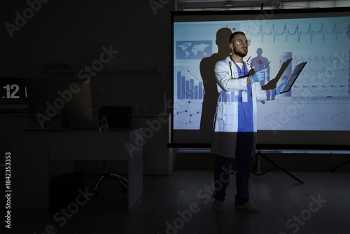 Male doctor with clipboard analyzing scientific data near projector screen in...