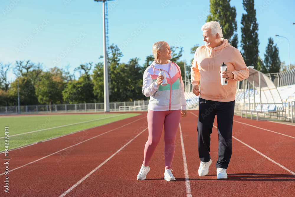 Obraz premium Sporty senior couple with water bottles training at stadium