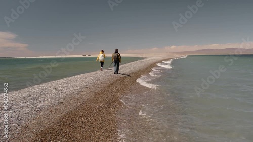 Beautiful view of a mountain lake with turquoise water and couple of tourists walking along a narrow sand spit. Gobi Desert, Mongolia, Mongol Els region. Outdoor activities, summer travel