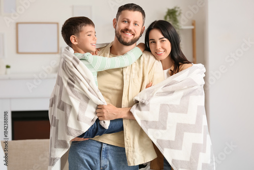 Happy parents and their little son with warm plaid hugging at home