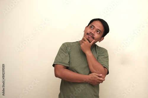 Portrait of a Southeast Asian man looking up with hand on chin, appearing thoughtful and curious. Isolated, great for ads or concepts.