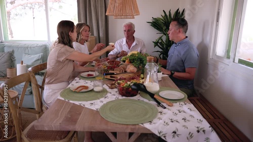 Happy multi generational family members gathering at the dining table, sharing food and drinks, and enjoying pleasant conversation during a delicious and healthy meal in a brightly lit room
