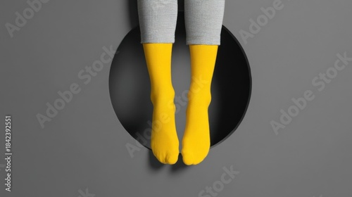A pair of feet wearing bright yellow socks dangle from a black circular object against a dark gray background,