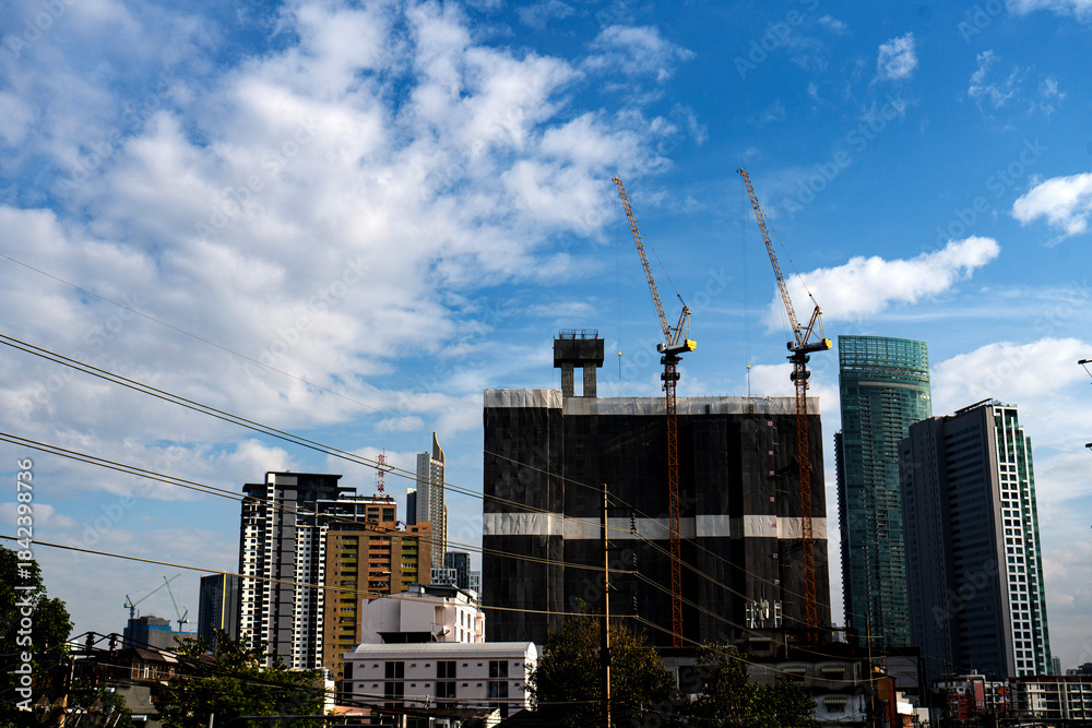 Fototapeta premium Towering construction cranes stand like mechanical giants beside a high-rise building
