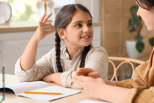 Little girl with her mother using sign language while doing homework in kitchen
