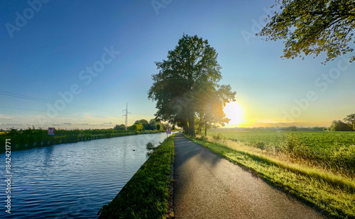 Photos Golden hour canal path bathed in warm sunlight, long tree shadows stretching acr