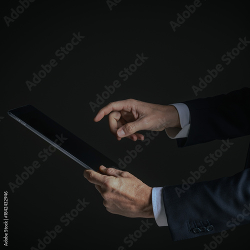 Side view of businessman hand pointing finger at a modern digital notepad isolated on dark background