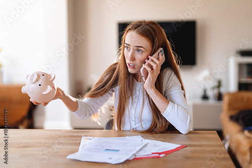 Canvastavla Woman talking on phone while holding piggy bank and looking concerned about fina