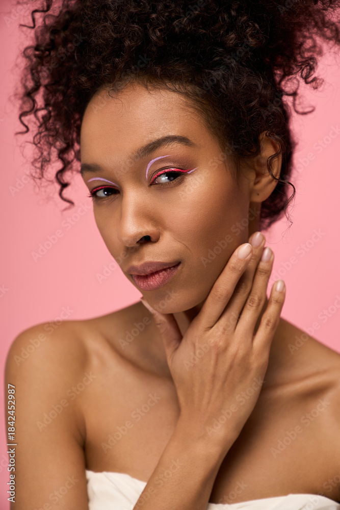 Fototapeta premium Young beautiful woman poses gracefully against a soft pink background, exuding charm and elegance