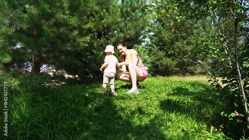 A mother walks with her baby in a beautiful garden filled with vibrant trees and soft grass