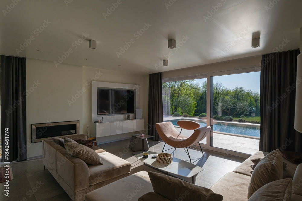 Obraz premium Modern luxury living room interior at sunset. Open-plan space featuring beige sofas, marble dining table, large glass windows with sun flare, and view of a patio. Stylish contemporary home design