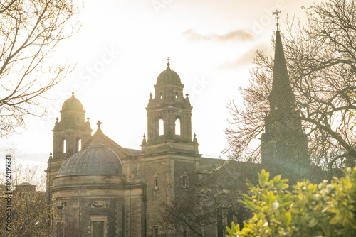 View of a golden sandstone tower of St John's Episcopal Church with Scottish flag fluttering atop, framed by the stark branches of winter trees, Edinburgh, Scotland, United Kingdom.