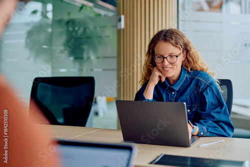 Canvas Print Woman with glasses smiling at a laptop screen in a bright corporate meeting room