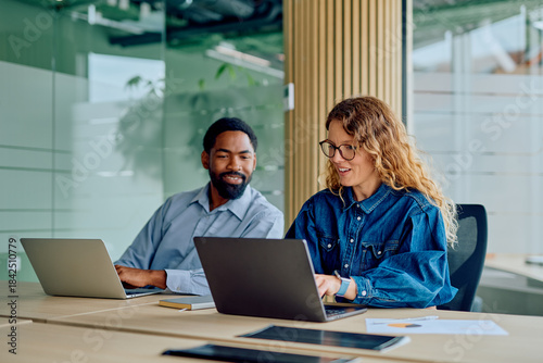 Tableau sur toile Two diverse colleagues smiling and working together on laptops at a modern offic