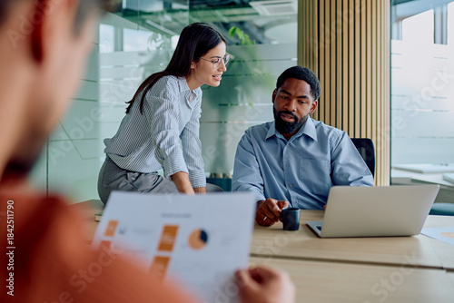 Diverse business people discussing financial charts and using laptop during an important corporate meeting in a glass boardroom