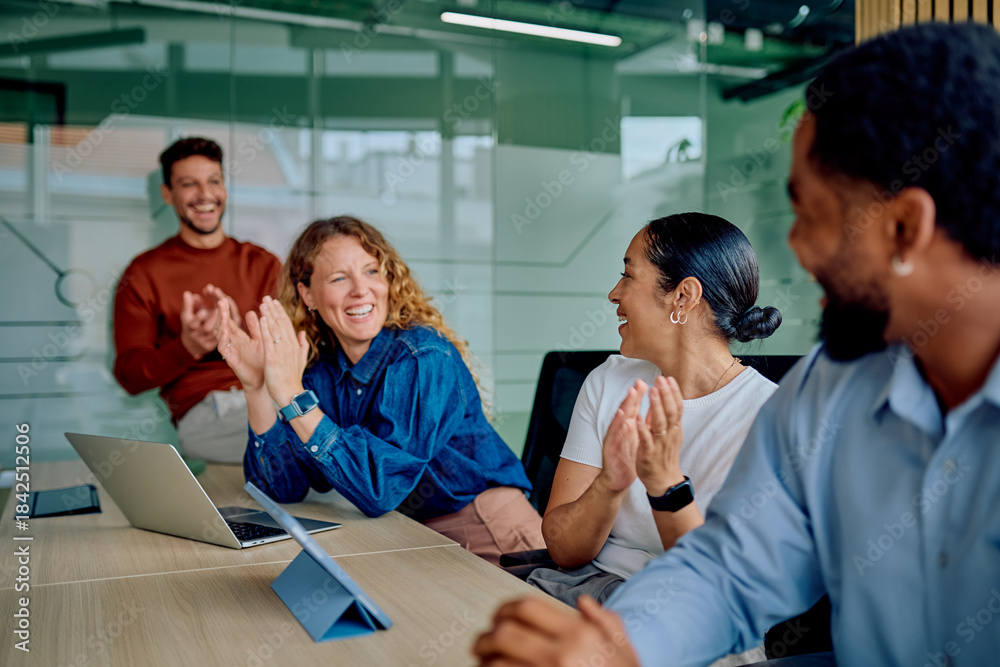 Fototapeta premium Diverse business professionals in an office meeting room, happily clapping and smiling during a celebration or successful presentation