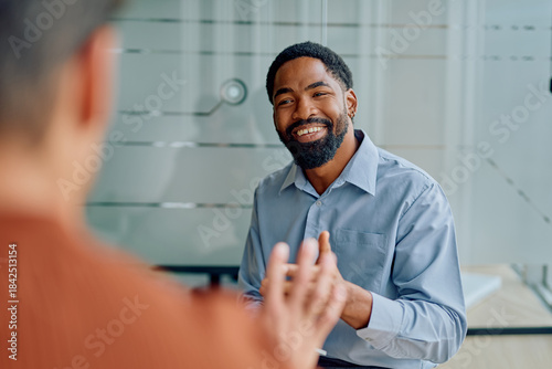 Fényképezés Young African American businessman smiling, listening, and communicating during
