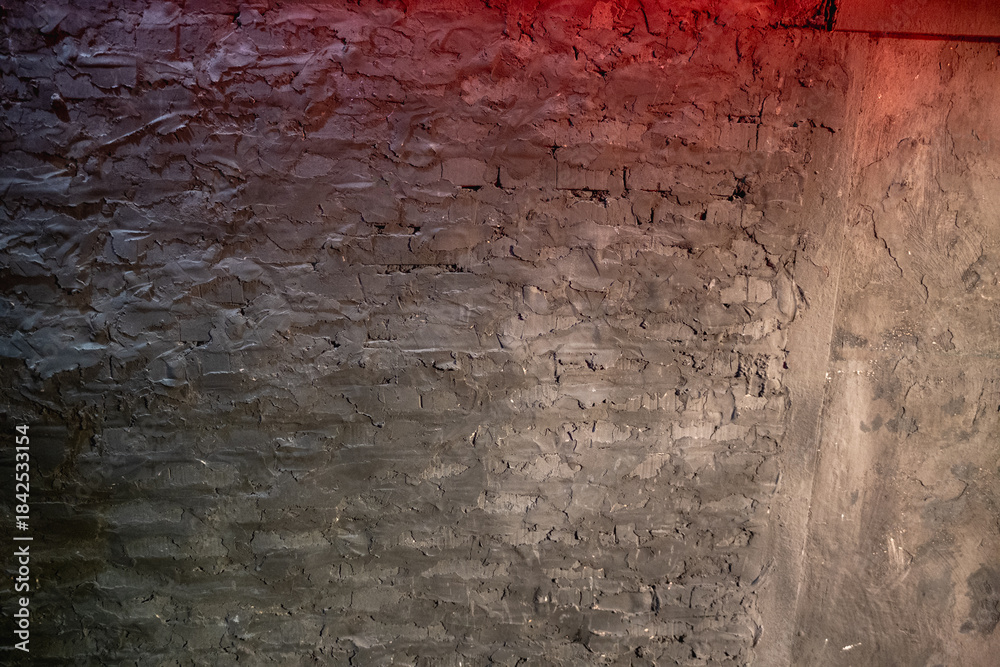 Obraz premium Dark rough texture on an old concrete wall and brick structure featuring uneven stucco, illuminated by a subtle red and orange gradient light, creating a grunge and industrial background