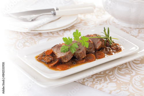 Goose meat stew with black pepper, served on a white platter.