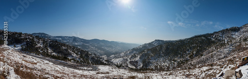 View of snow-dusted mountains and winding roads under a bright sun, a serene winter landscape in Murree, Punjab, Pakistan.