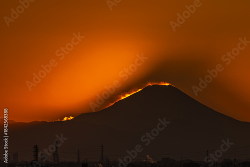 夕陽に輝く雪煙と山影を映すシルエットの富士山