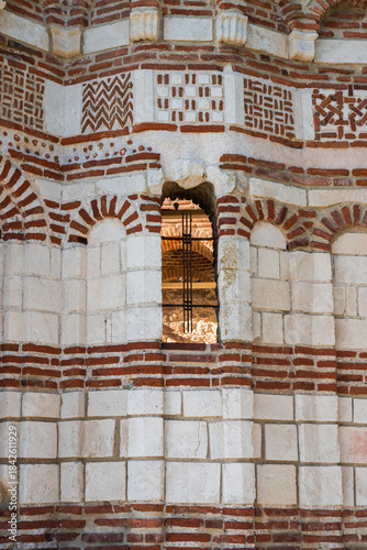 Bild auf Leinwand A narrow arched window framed by intricate brickwork pierces a historic wall of alternating stone and brick
