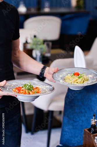 Close-up of restaurant staff serving freshly prepared pasta dishes on elegant plates inside a modern restaurant. Focus on plated food and professional service